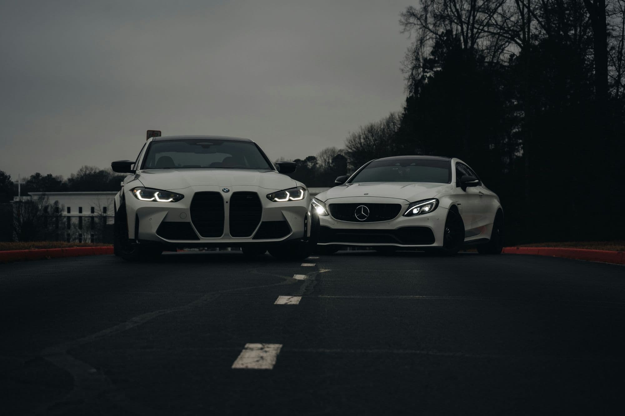 Two white cars on the road at dusk, headlights on